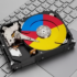 Hard disk drive resting on a silver laptop keyboard with a multicolored, Google-style circular label on the platter.