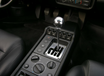 Interior of a black car showing a chrome manual gear shifter, center console with buttons and climate controls.