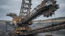 Massive bucket-wheel excavator in an open-pit mine with conveyors and a dusty, gray sky.