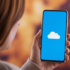 Person holding a smartphone displaying a white cloud icon on a blue screen