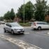 Silver Renault hatchback in the foreground navigating a wet roundabout, with other cars and brick row houses with trees in the background.