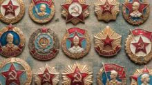 A collection of Soviet-era medal pins featuring red stars, gold wreaths, and hammer-and-sickle symbols on textured fabric.