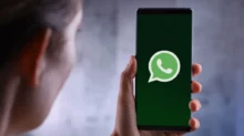 Hand holding a smartphone showing the WhatsApp logo on a dark green screen