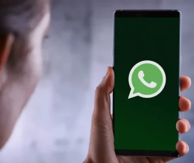 Hand holding a smartphone showing the WhatsApp logo on a dark green screen