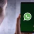 Hand holding a smartphone showing the WhatsApp logo on a dark green screen
