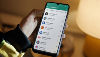 Person holding a smartphone displaying a social app's Discovery Feed with avatars and follower counts.