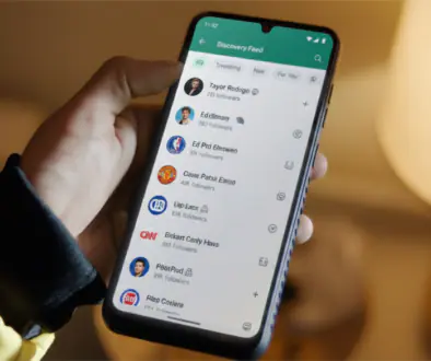 Person holding a smartphone displaying a social app's Discovery Feed with avatars and follower counts.