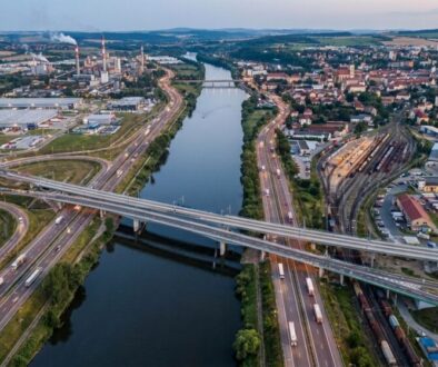 Aerial view of a river with multiple bridges, highways and a rail yard, separating an industrial area from a residential town.