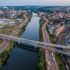 Aerial view of a river with multiple bridges, highways and a rail yard, separating an industrial area from a residential town.