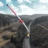A giant red-and-white wind turbine blade spans a rural road, supported by trucks amid hills and forests.