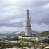 Tall tower with guy wires rising above a cluster of low industrial buildings in a snow-covered, desolate landscape under a cloudy sky.