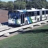 Articulated city bus travelling on an elevated concrete guideway beside a grassy area, with trees in the background.