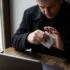 Man in a dark coat at a café table, holding a credit card next to a laptop and a coffee cup on the table.