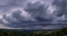 Dark storm clouds loom over rolling countryside with a small village in the valley.