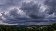 Dark storm clouds loom over rolling countryside with a small village in the valley.