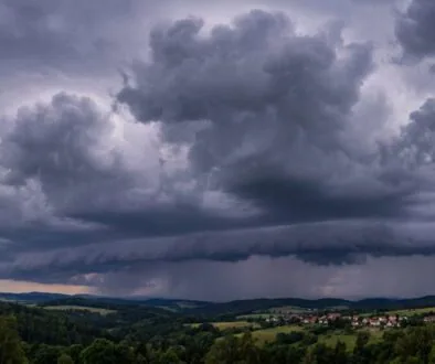 Dark storm clouds loom over rolling countryside with a small village in the valley.