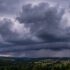 Dark storm clouds loom over rolling countryside with a small village in the valley.