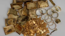 Pile of tarnished gold items: bars, coins, and circular jewelry on a gray background (antique treasure)