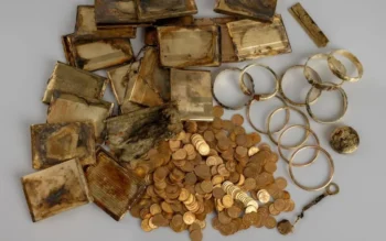 Pile of tarnished gold items: bars, coins, and circular jewelry on a gray background (antique treasure)