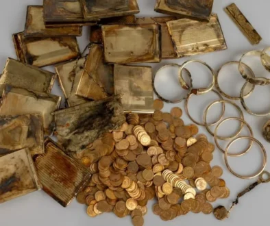 Pile of tarnished gold items: bars, coins, and circular jewelry on a gray background (antique treasure)