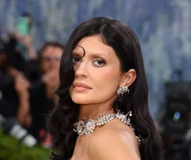 Elegant woman on the red carpet wearing an elaborate pearl necklace and earrings, photographers in the background.