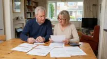 Couple reviewing several documents at a wooden dining table in a living room, using a calculator nearby.