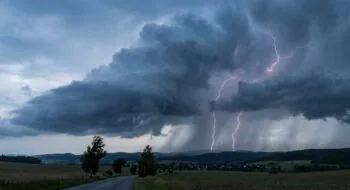 Dark storm clouds over a rural landscape with a winding road; bright lightning bolts strike near the horizon.