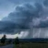 Dark storm clouds over a rural landscape with a winding road; bright lightning bolts strike near the horizon.