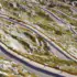 Winding mountain road with sharp switchbacks and wooden guardrails along rocky, grassy slopes.