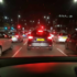 Nighttime city traffic from a car’s dashboard view; red brake lights and cars ahead on a multi-lane road.