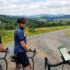 Three cyclists on a rural gravel road, one glancing back as the third rider checks a map on a phone mounted to a handlebar.
