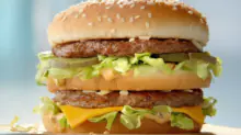 Double cheeseburger with sesame bun, two beef patties, lettuce, pickles, and melted cheese on a paper-wrap surface.