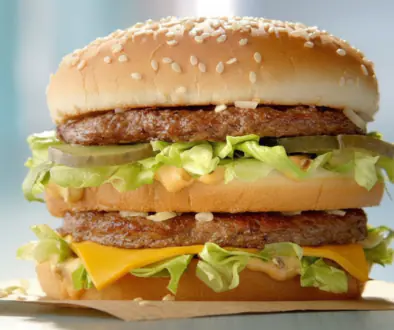 Double cheeseburger with sesame bun, two beef patties, lettuce, pickles, and melted cheese on a paper-wrap surface.