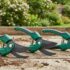Three green hand pruners with curved blades lying on a wooden surface in a garden day.