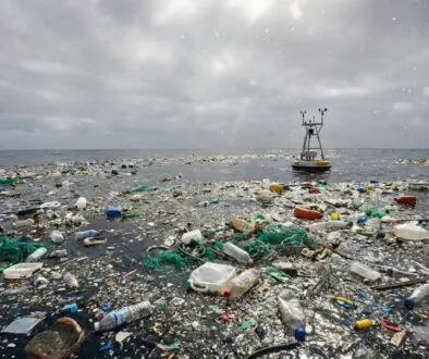 Ocean surface littered with plastic bottles, bags, nets and debris under a cloudy sky, with a small platform in the distance
