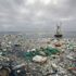 Ocean surface littered with plastic bottles, bags, nets and debris under a cloudy sky, with a small platform in the distance