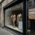 Storefront window displaying three beige suits on mannequins; taped 'GESCHLOSSEN' sign indicates the shop is closed.