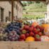 Wooden crate of fresh fruit—green and purple grapes, strawberries, and oranges at an outdoor market.