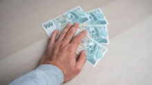 Člověku pod rukou leží české bankovky.