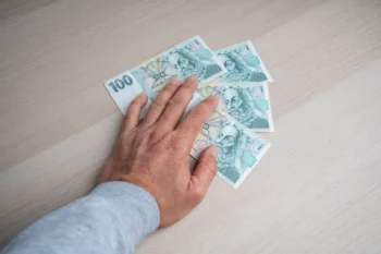 Člověku pod rukou leží české bankovky.
