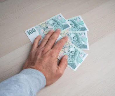 Člověku pod rukou leží české bankovky.