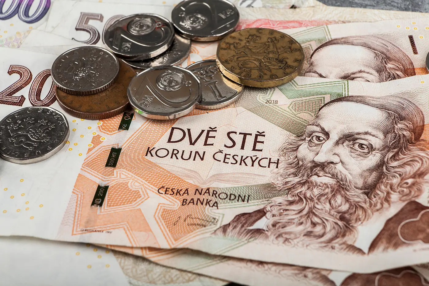 Na stole leží české papírové bankovky a na nich také české mince